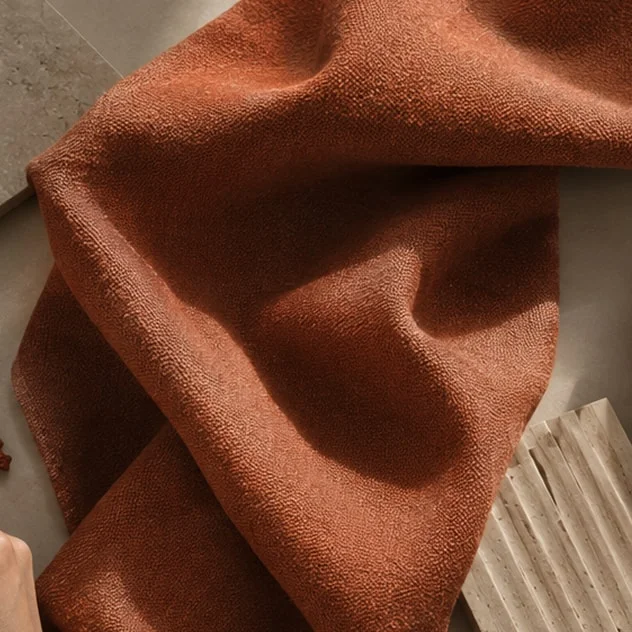 Close-up of draped terracotta wool fabric beside a fluted stone sample