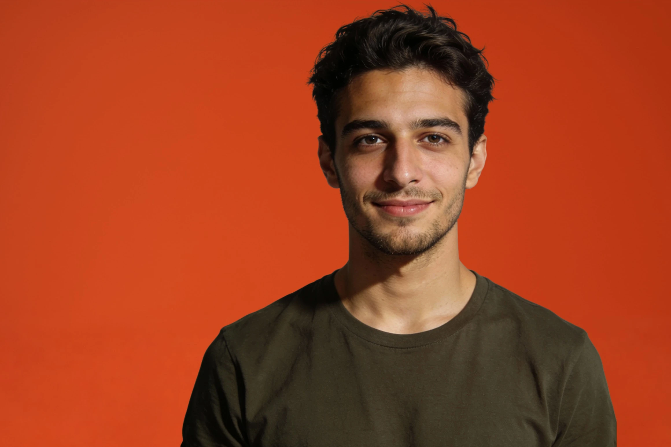 Portrait of Tomás Reyes with short dark hair in an olive-green T-shirt against a vermilion backdrop